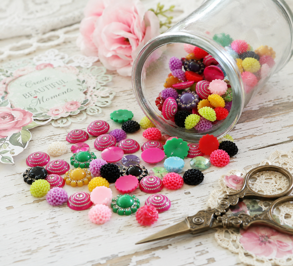 Colourful resin cabochon embellishments for scrapbooking, card making, junk journals and mixed media projects displayed on a shabby white craft table.